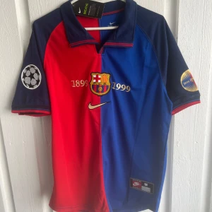 Barcelona Rivaldo 1899-1999 tröja Nike M - Säljer en ikonisk FC Barcelona fotbollströja från Nike, Rivaldo #11, jubileumsmodell 1899-1999. Tröjan är röd och blå med guldiga detaljer, klubbmärke och Champions League-patch på ärmarna. Klassisk krage och korta ärmar. Perfekt för samlare eller fans!