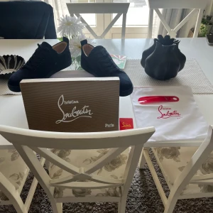 Mörkblå sneakers från Christian Louboutin - Snygga mörkblå sneakers från Christian Louboutin i mocka med ton-i-ton snörning och diskret broderad logga på hälen. Skorna har en klassisk låg siluett och svart sula, samt beige innersida i skinn. Perfekta för dig som gillar stilrena och exklusiva sneakers. Aldrig använda eller testade säljer då de blev fel storlek.