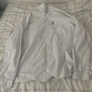 Vit skjorta från Free Wear 158/164 - Klassisk vit skjorta från Free Wear i storlek 158/164. Skjortan har lång ärm, bröstficka och knäppning framtill. Perfekt till skjorta-looken med krage och enkel stil. Tillverkad i mjukt bomullstyg för en bekväm känsla.