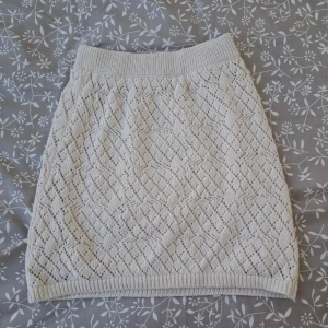 Benvit stickad kjol från Gina Tricot - Supersöt benvit stickad kjol från Gina Tricot i kort modell. Kjolen har ett snyggt hålmönster och bred resår i midjan för extra komfort. Perfekt att styla med en enkel topp eller en oversized stickad tröja.