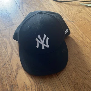 Svart New Era Yankees keps - Klassisk svart New York Yankees keps från New Era med broderad vit NY-logga framtill och MLB-logga bak. Kepsen är i modellen fitted och tillverkad i 100% polyester. Perfekt för dig som vill ha en clean och sportig stil.