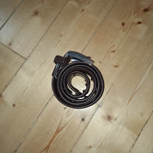 Brunt skärp i skinn 100cm - Snyggt brunt bälte i  skinn med klassiskt silverfärgat spänne. Bältet är justerbart och nickel-fritt, perfekt för dig som vill ha en stilren accessoar till jeans eller byxor. Enkel design utan mönster och med robust känsla.