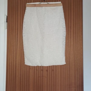 Vit spetskjol med rak passform - Snygg vit kjol i rak modell med vacker spets över hela tyget. Kjolen är knälång och har en feminin känsla med sitt spetsmönster. Perfekt att styla med en enkel topp och sneakers eller boots.