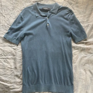 Blå pikétröja från Dressmann Premium - Säljer en stilren blå pikétröja från Dressmann Premium. Tröjan har klassisk krage, två knappar och korta ärmar. Materialet känns mjukt och är stickat. Storlek S. Bra skick! Lite använd och inga defekter. 