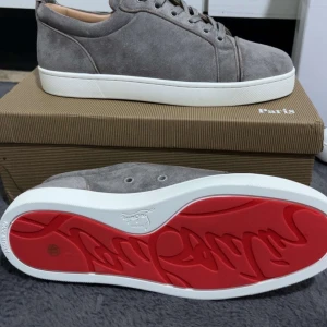 Loboutin skor - Snygga grå sneakers i mocka från Christian Louboutin med klassisk vit sula och den ikoniska röda undersidan. Skorna har rund tå, snörning och stilren design som passar perfekt till streetwear eller en clean look.