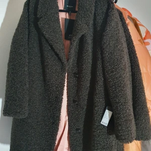 Brun teddyjacka Rockandblue stl 44 - Mysig brun teddyjacka från Rockandblue i storlek 44. Jackan har en fluffig, fårullsinspirerad yta, knäppning framtill med knappar och ljusrosa foder. Perfekt för kalla dagar när du vill vara både varm och snygg.