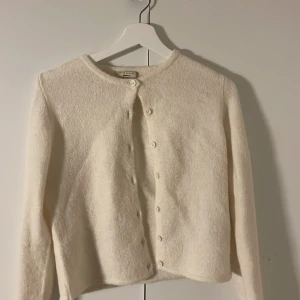 Vit kofta från Gina Tricot XS - Supermjuk och fluffig vit kofta från Gina Tricot i storlek XS. Koftan har rund halsringning, långa ärmar och knäpps med små vita knappar framtill. Perfekt för lager-på-lager och en clean look.