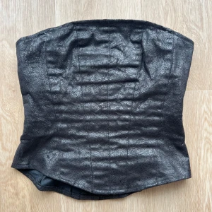 Svart korsett i skinnimitation - Cool svart korsett i skinnimitation med markerade sömmar och dragkedja i sidan. Axelbanden är utbytbara och har begie utsida.