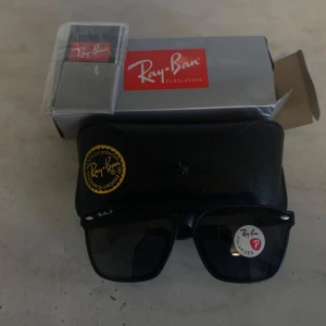 Svarta Ray-Ban Wayfarer solglasögon - Snygga svarta Ray-Ban Wayfarer solglasögon med polariserade glas. Klassisk fyrkantig form och diskret logga på skalmen. Kommer med originalfodral och box. Perfekta för dig som vill ha en tidlös och cool look.