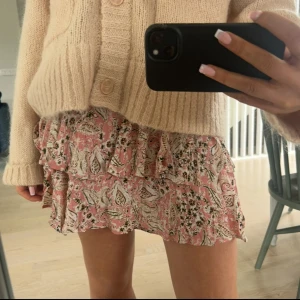 Rosa volangkjol med blommigt mönster - Supersöt kort kjol i rosa med blommigt mönster och volanger. Kjolen har flera lager och en flowy känsla, perfekt för en chill och feminin look. Passar snyggt med stickad tröja eller crop top. Bekväm och lätt att bära.