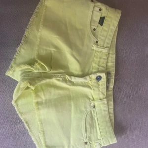 Gula jeansshorts från Pull&Bear - Snygga ljusgula jeansshorts från Pull&Bear med råa kanter och klassisk femficksdesign. Shortsen har knapp och dragkedja framtill samt bälteshällor. Perfekta för sommardagar.