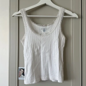 Vit spetskantad topp Brandy Melville - Supersöt vit linnetopp från Brandy Melville med ribbad struktur och små broderade detaljer. Spetskant runt halsringning och axelband ger en romantisk vibe. Har deofläckar som knappt syns❤️