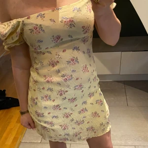 Gul blommig kortklänning från MNG - Supersöt gul kortklänning från MNG med små blommor i rosa och blått. Klänningen har puffärmar som kan bäras både offshoulder och på axeln, samt en smickrande fyrkantig ringning. Perfekt för sommarens alla tillfällen!