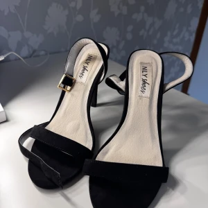 Svarta klackar från NLY Shoes - Eleganta klackar från NLY Shoes – storlek 36  Stilrena svarta klackar med smal remdesign och gulddetalj vid spännet. Passar perfekt till fest, bröllop eller en fin middag. Enkla att matcha med både klänning och byxdress!  ✔️ Klassisk och tidlös modell ✔️ Endast använda enstaka gång ✔️ Bra skick  Pris innan: 499 Pris nu: 175