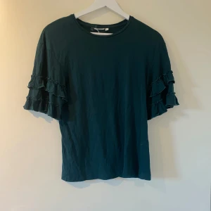 Mörkgrön topp med volangärmar - Super söt tröja som är något mer grön i värkligheten. Den har ett litet litet hål uppe bredvid lappen. Jag har tyvärr ingen aning om vart tröja är i från då lappen är bortklippt💗
