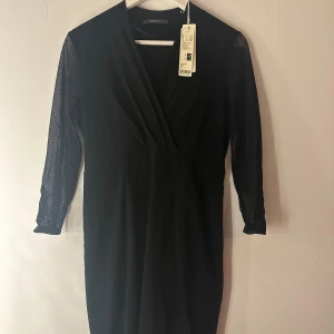Svart klänning från Esprit - Svart klänning från Esprit med trekvarts transparenta ärmar och markerad midja. Klänningen har v-ringning och är tillverkad i ett mjukt material som ger en snygg siluett. Perfekt för dig som gillar stilrena och klassiska plagg.