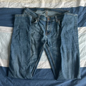 Ljusblå nudie jeans - Säljer ett par ljusblå jeans från Nudie Jeans Co i klassisk femficksmodell. Jeansen har raka ben, snygga kontrastsömmar och Nudie-logga på bakfickan. Perfekta för dig som gillar en clean och tidlös look.