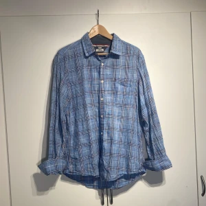 Blå rutig skjorta Tommy Hilfiger - Snygg blå rutig skjorta från Tommy Hilfiger i bomull. Skjortan har klassisk krage, bröstficka och vita knappar framtill. Perfekt för dig som gillar en avslappnad men ändå stilren look. Storlek L. Välanvänd men i fint skick. 
