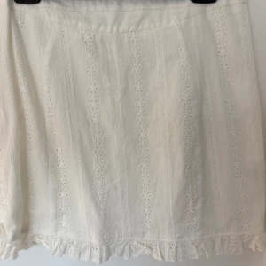 Vit broderad kjol från Tiger Mist - Superfin vit kortkjol från Tiger Mist med broderade blommor och volangkant nertill. Kjolen har dragkedja i sidan och är gjord i bomull. Är mer som M. Knappt använd. 