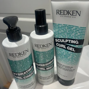 Redken Curl Styling Kit - Säljer ett kit från Redken med Hydrating Curl Cream, Refreshing Curl Mist och Sculpting Curl Gel. Produkterna är i vita och svarta plastflaskor med turkos text och är perfekta för att definiera och återfukta lockigt hår. Innehåller jojobaolja och ger glans och stadga. Cirka 80 procent kvar i flaskorna. 