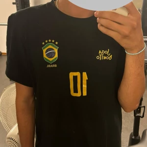 Svart Brasilien fotbollströja nr 10 - Snygg svart fotbollströja med Brasiliens emblem, texten 'Joga Bonito' och nummer 10 . Perfekt för dig som älskar fotboll och vill sticka ut med en unik design. Storlek L 