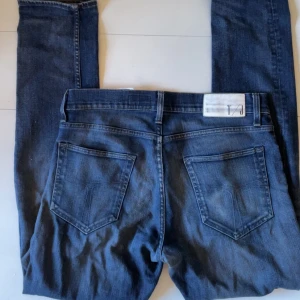 Tiger of Sweden jeans - Snygga blå jeans från Tiger of Sweden med klassisk femficksdesign och raka ben. Jeansen har en mörk tvätt med lätt slitning och tydliga sömmar på bakfickorna. Perfekta för dig som gillar en enkel och stilren look. Jeansen är lite insydda på sidan och passar storleken 32/32.