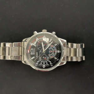Svart och silverfärgad Quartz klocka  - Stilren klocka från IKABO med svart urtavla, silverfärgat armband i metall och flera små urtavlor för extra funktioner. Snygga detaljer i rött och vitt på urtavlan ger en sportig känsla. Perfekt accessoar för dig som gillar en modern look.