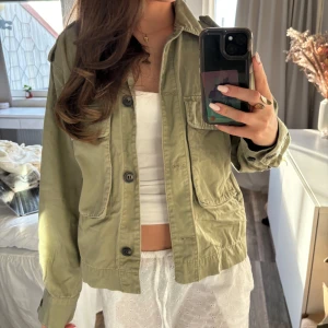 Olivgrön utilityjacka med knappar - Säljer en olivgrön utilityjacka med klassisk krage och stora fickor framtill. Jackan har knäppning med knappar och är långärmad. Perfekt för lager-på-lager och enkel att styla till olika outfits. Passar allt från Xs-M❤️