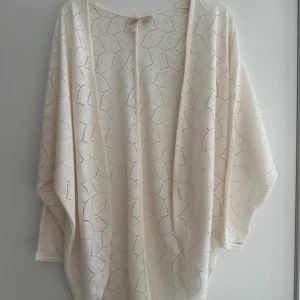 Creamvit stickad kofta. Funkar även som cover-up till stranden - Superfin vit stickad kofta med öppet mönster och lös passform. Perfekt att slänga över en topp för en chill och stilren look eller som cover-up till stranden. Koftan har vida ärmar och ett snyggt mönster
