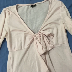 Ljusrosa omlottopp från Gina Tricot - Supersöt ljusrosa omlottopp från Gina Tricot med knyt framtill och djup v-ringning. Toppen har långa ärmar och är gjord i mjuk bomullsmix, perfekt för en chill och trendig look.