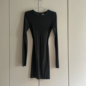 Mörkgrå långärmad klänning H&M Divided - En stilren mörkgrå kortklänning från H&M Divided. Klänningen har lång ärm, rund halsringning och en figurnära passform. Perfekt för dig som gillar en enkel och clean look. Materialet är mjukt och stretchigt för extra komfort.