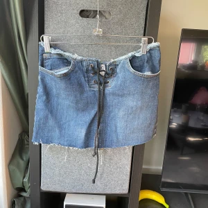 Jeanskjol BDG Urban outfitters - Lågmidjade jeanskjol!!! Snygg blå jeanskjol från BDG Urban Outfitters med snörning framtill och rå, fransig kant upptill och nedtill. Klassiska fickor fram och bak, perfekt för en cool och avslappnad stil.