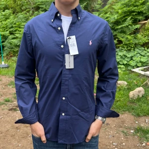 Ny blå Ralph Lauren skjorta - Säljer denna stilrena och snygga blå Ralph Lauren skjorta. Skjortan är helt ny, aldrig använd och har alla lappar kvar, till och med prislappen från Best of Brand där nypriset är 999 kr. Modellen är M slim fit. Har du några frågor? Tveka inte att höra av dig. Allt gott från Deluxe garderoben.