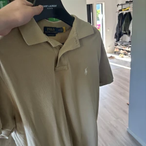 Beige pikétröja från Polo Ralph Lauren M - Säljer en beige pikétröja från Polo Ralph Lauren i custom slim fit. Klassisk krage, kort ärm och broderad vit logga på bröstet. Tillverkad i bomull och perfekt för en clean och stilren look.