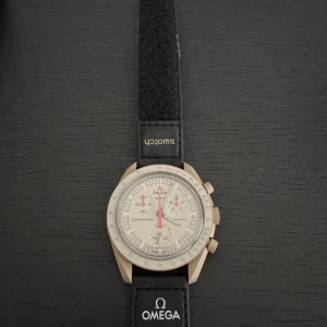 Omega x Swatch Speedmaster MoonSwatch - Säljer en Omega x Swatch Speedmaster MoonSwatch med svart textilband och vit urtavla. Klockan har kronograf, tachymeter och röda detaljer på visarna. Snygg och ikonisk design, levereras med originalbox och certifikat.
