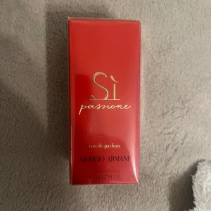 Armani Sì Passione EdP 50 ml - Armani Sì Passione Eau de Parfum i 50 ml flaska. Parfymen kommer i en snygg röd kartong med gulddetaljer och svart text. Doften är känd för sin fruktiga och blommiga karaktär, perfekt för dig som gillar eleganta och intensiva parfymer.