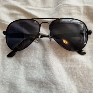 Svarta aviator solglasögon - Snygga svarta aviator solglasögon med mörka glas och tunna metallbågar. Klassisk pilotform med näskuddar för extra komfort. Perfekt accessoar för en cool look i solen.