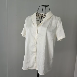 Vit kortärmad skjorta med knappar - Stilren vit skjorta med korta ärmar och klassisk krage. Skjortan har knäppning framtill med vita knappar och är tillverkad i ett lätt och mjukt material som känns skönt mot huden. 