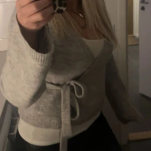 Ljusgrå omlottkofta med knytband - Supermysig ljusgrå stickad omlottkofta med knytband i midjan och v-ringning. Koftan har långa ärmar och en loose passform, perfekt att slänga på sig över ett linne eller t-shirt. Enkel och stilren look som funkar till det mesta. Från Gina, st M men sitter bra på mig som är S  