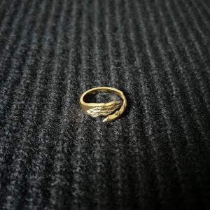 Fusion Sauvage Dorée – Wild Fusion Ring - Justerbar ring i rostfritt stål med guldplätering, rost- och nickelfri. En vinge och svanslik kurva förenas i asymmetrisk form – balanserad kontrast med rörelse och karaktär