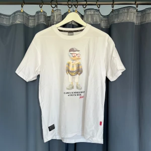 Vit t-shirt Duck Dude - Vit t-shirt från B-One-Soul med coolt tryck av en anka i streetwear-stil och texten 'EARLY SUMMER PREP of DUCK DUDE'. Klassisk passform, rund hals och korta ärmar. Perfekt för dig som gillar unika prints och avslappnad stil. Street version av Ralph Lauren teddybjörnen (; köpt i Japan