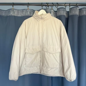 Beige pufferjacka från & Other Stories - Snygg beige pufferjacka från & Other Stories med hög krage och två stora fickor framtill. Jackan har dragkedja och en lite boxig, loose passform som ger en chill vibe. Perfekt för kalla dagar när du vill vara både varm och stilren.