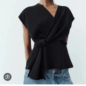 Svart omlottopp med knyt - Slutsåld.                                                    Populär stilren svart omlottopp med knyt i midjan och v-ringad hals. Toppen har korta ärmar. Perfekt att matcha med jeans eller kjol för en trendig look