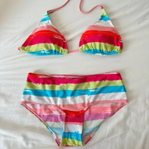 Färgglad randig bikini med knyt - Superfin bikini med färgglada ränder i rosa, rött, blått, grönt och vitt. Överdelen är trekantsmodell med knyt i nacken och ryggen, och underdelen är midjehög. Perfekt för strandhäng och poolparty! Materialet är mjukt och stretchigt syntet. Båda delarna är i storlek 38/40