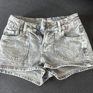 Grå jeansshorts från h&m storlek 158 - Snygga grå jeansshorts från h&m med hög midja och två knappar framtill. Shortsen har stora framfickor och bakfickor med broderade hjärtan. Tillverkade i mjukt denimtyg, perfekta för sommardagar. Passar dig som gillar en avslappnad men trendig stil. Storlek 158