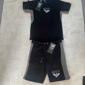 Svarta och grå shorts från Gravity Grab - Shorts från Gravity Grab i svart med gråa paneler på sidorna. De har snörning i midjan och en broderad Gravity Grab-logga framtill. Perfekta för en chill och sportig stil. Materialet känns mjukt och bekvämt, troligen bomull eller polyester.