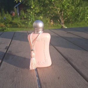 Parfym Delina från Parfums de Marly - Delina Eau de Parfum, 75 ml, från Parfums de Marly. Flaskan är matt ljusrosa med silverfärgad rund kork och dekorativ tofs. Vackra detaljer i relief på flaskan ger en lyxig känsla. Kommer i matchande rosa kartong. Den är helt ny, inte använd. Säljer då jag inte tyckte det var min doft