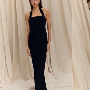 Svart långklänning med halterneck - Supersnygg svart långklänning med halterneck och rak urringning. Klänningen har en figurnära passform och draperad midja som ger en elegant siluett. Perfekt för dig som vill sticka ut med en klassisk och stilren look.