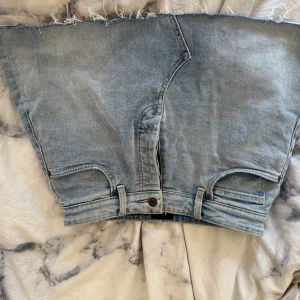 Ljusblå jeanskjol från Lee - Säljer en ljusblå jeanskjol från Lee med rå kant och klassiska fickor både fram och bak. Kjolen har bälteshällor, knapp och dragkedja framtill samt Lee-broderi på bakfickan. Perfekt för dig som gillar en avslappnad och trendig denimlook. Har en liten fläck som knappt syns bild 2 