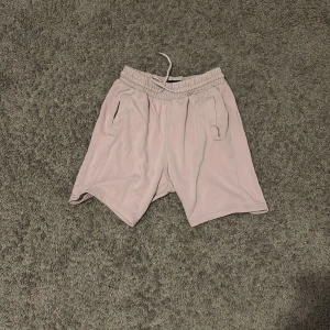 Ljusrosa shorts med snörning HM - Säljer ett par ljusrosa shorts med elastisk midja och snörning framtill. Shortsen har två sidofickor och en bakficka, perfekta för chill dagar. Tillverkade i mjukt material som känns skönt mot huden.